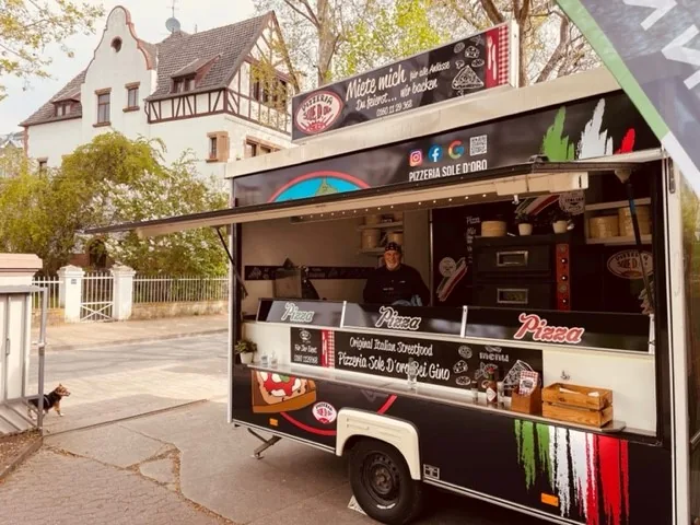 Der Pizzawagen Sole D'Oro — geöffnet, mit Pizzaiolo am Holzofen